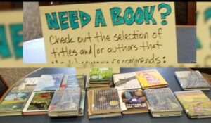 Table with sign that says "Need a Book? Check out thes authors and titles that Mr. ____ recommends" with a number of books face up on the table. 